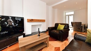 Ein modernes Wohnzimmer mit Flachbildfernseher, Ledersofa, Couchtisch aus Holz und einem Essbereich mit Tisch und Stühlen.