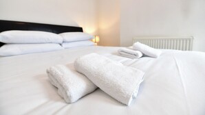 Ein ordentlich bezogenes Bett mit weißen Leinen und Handtüchern, eine Nachttischlampe und ein weißer Heizkörper.