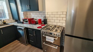 A modern kitchen with black cabinets, a stainless steel stove, a red toaster, and a black dishwasher. - Newly refurbished One Bedroom House With Front Garden (London)