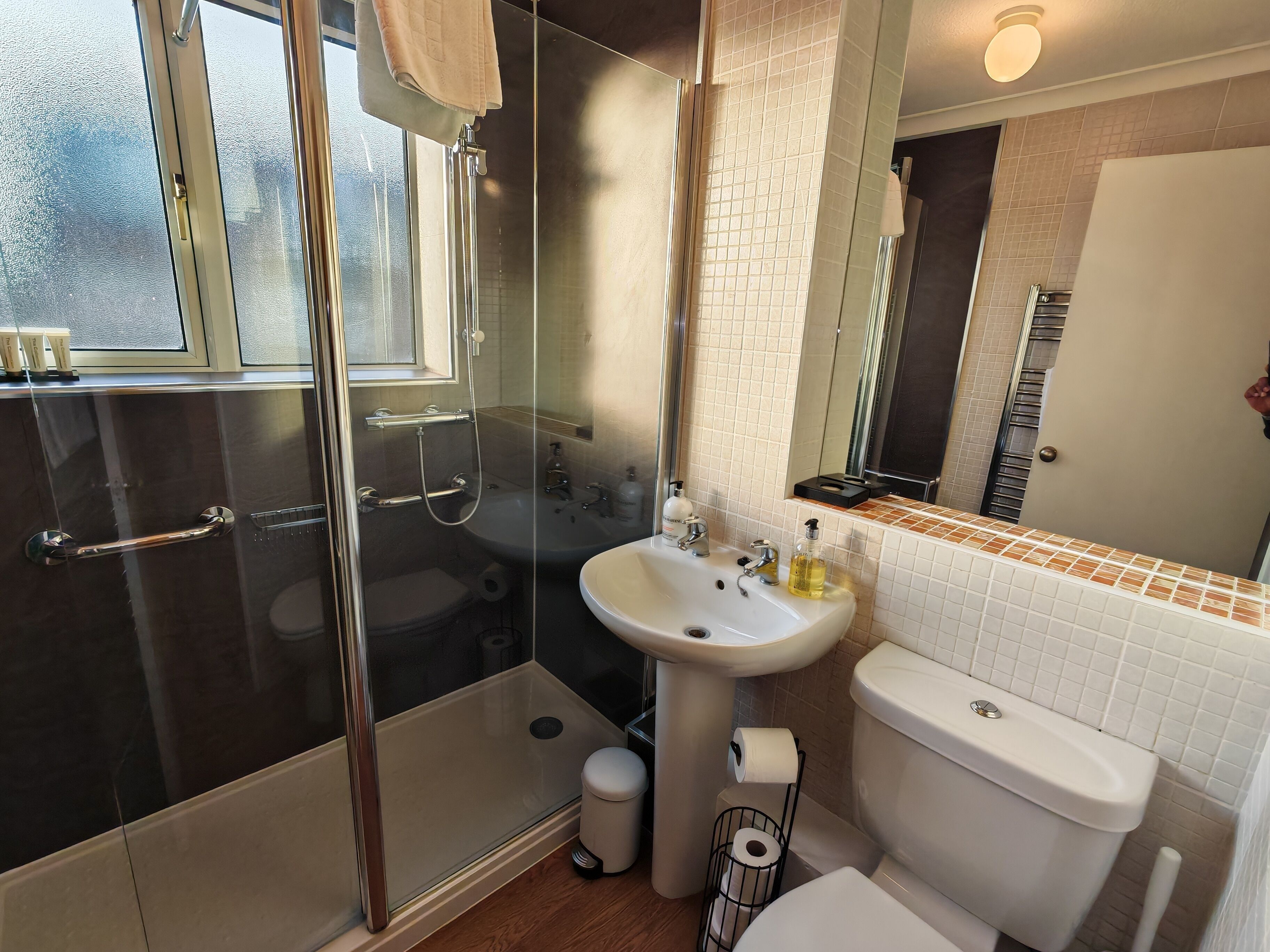 Ein modernes Badezimmer mit einer gläsernen Duschkabine, einem Waschbecken inklusive Spiegel und einer Toilette.