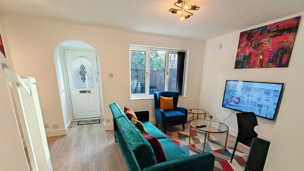 A modern living room with a teal sofa, a blue armchair, a glass coffee table, and a TV mounted on the wall. - Newly refurbished One Bedroom House With Front Garden (London)