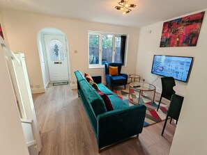 Un salon moderne avec un canapé de couleur turquoise, un fauteuil bleu, une table basse en verre et un téléviseur fixé au mur.