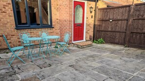 A patio with a brick wall, a red door, and a wooden fence. - Newly refurbished One Bedroom House With Front Garden (London)