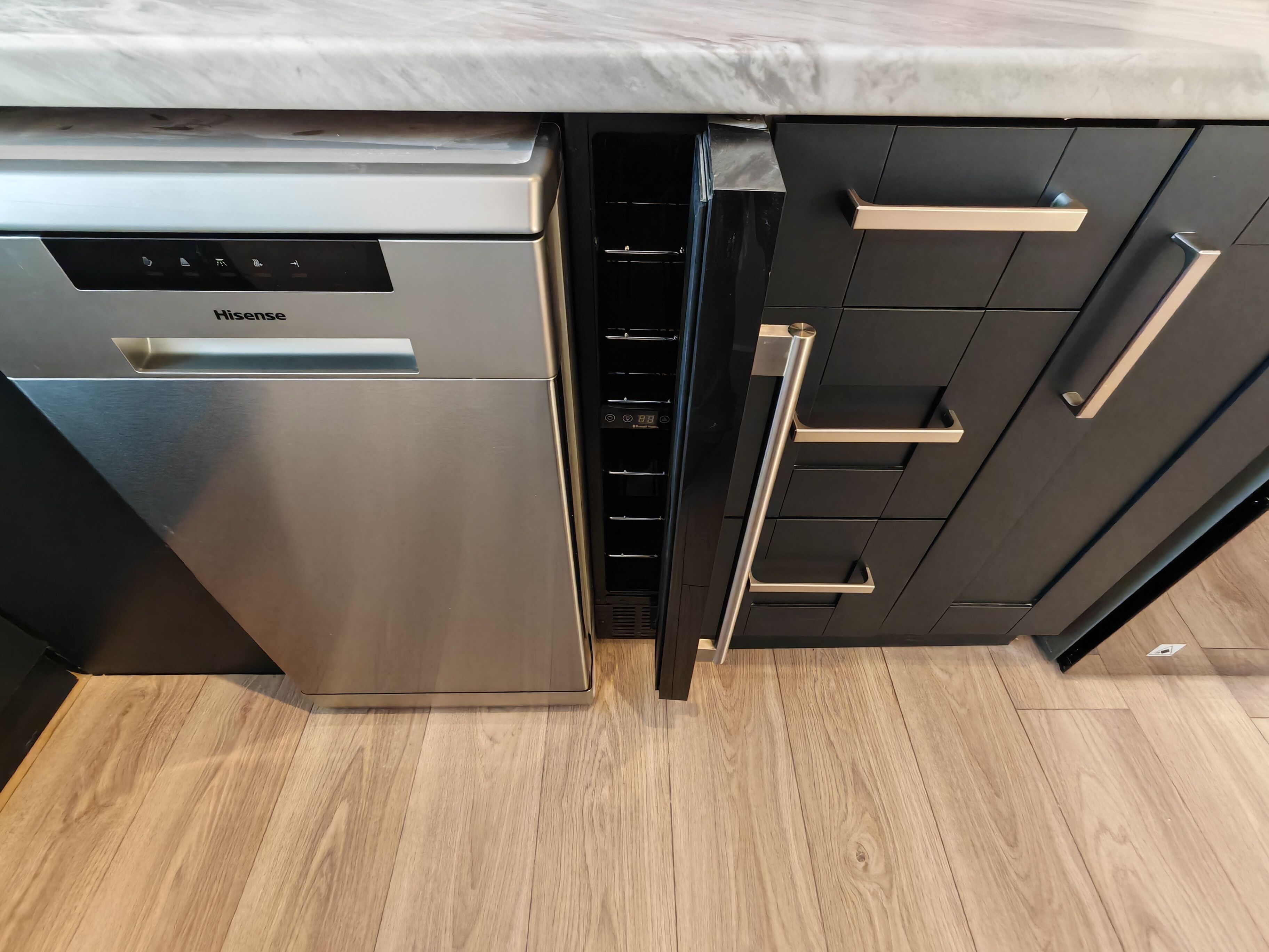 A kitchen with a stainless steel dishwasher, black cabinets, and a wooden floor.
