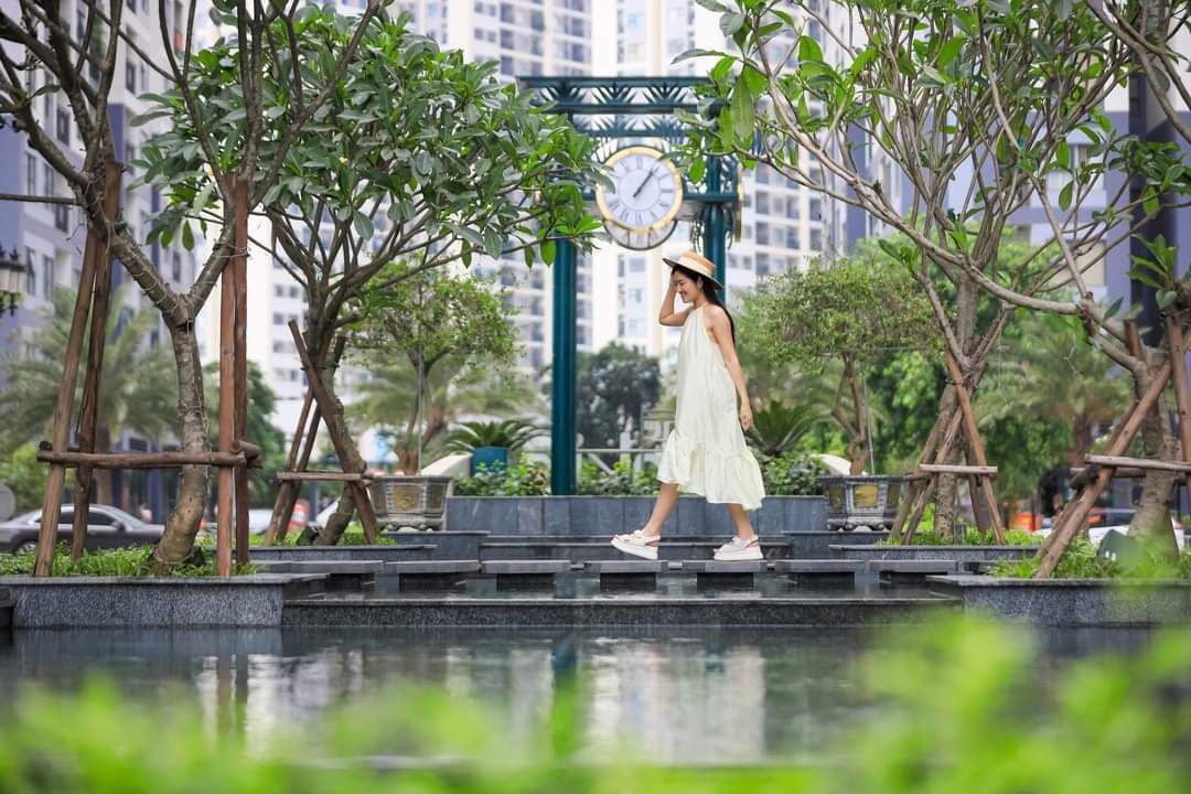 A woman walking on a bridge with a clock and greenery in the background.