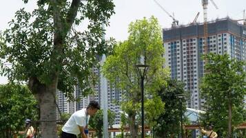 A golf course with a person playing, surrounded by trees and a building under construction in the background.