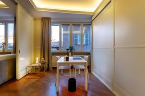 A dining area with a white table and chairs, a glass coffee table, a black trash bin, and a window with curtains. - CAVOUR SUITE LUXURY 7, located in Galleria Cavour, Bologna's historic center. (Bologna)