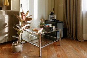 A modern living room with a glass coffee table, a potted plant, a small side table with a coffee machine, and a sofa. - CAVOUR SUITE LUXURY 7, located in Galleria Cavour, Bologna's historic center. (Bologna)