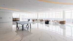 Een ruime, moderne lounge met een tafeltennistafel, comfortabele zitplaatsen en grote ramen met uitzicht.