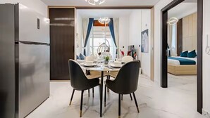 Een moderne eetruimte met een roestvrijstalen koelkast, een kroonluchter en een eettafel gedekt voor vier personen.
