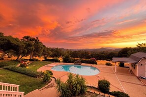 Ein Garten mit Schwimmbecken, umgeben von gepflegten Rasenflächen und Bäumen, unter einem Abendhimmel.