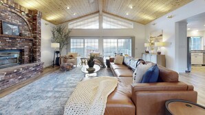 A spacious living room with a fireplace, leather sofa, and a high ceiling with wooden beams. - 'Whispering Oaks Estate' w/ Pool & View in Murphys (Murphys)