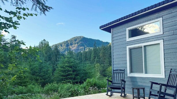 Une terrasse en bois avec deux fauteuils à bascule et une petite table, offrant une vue sur une montagne boisée.