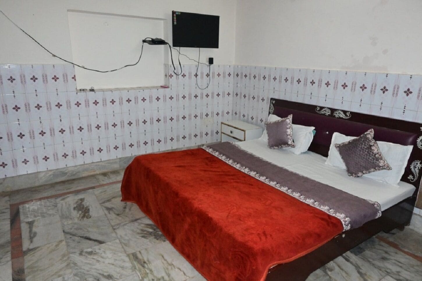 A bedroom with a bed, a TV mounted on the wall, and patterned wallpaper.