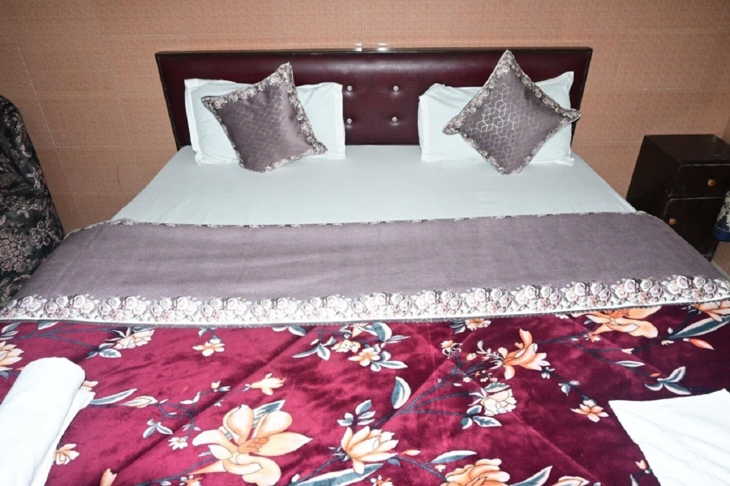A bed with a floral-patterned bedspread, two decorative pillows, and a headboard.