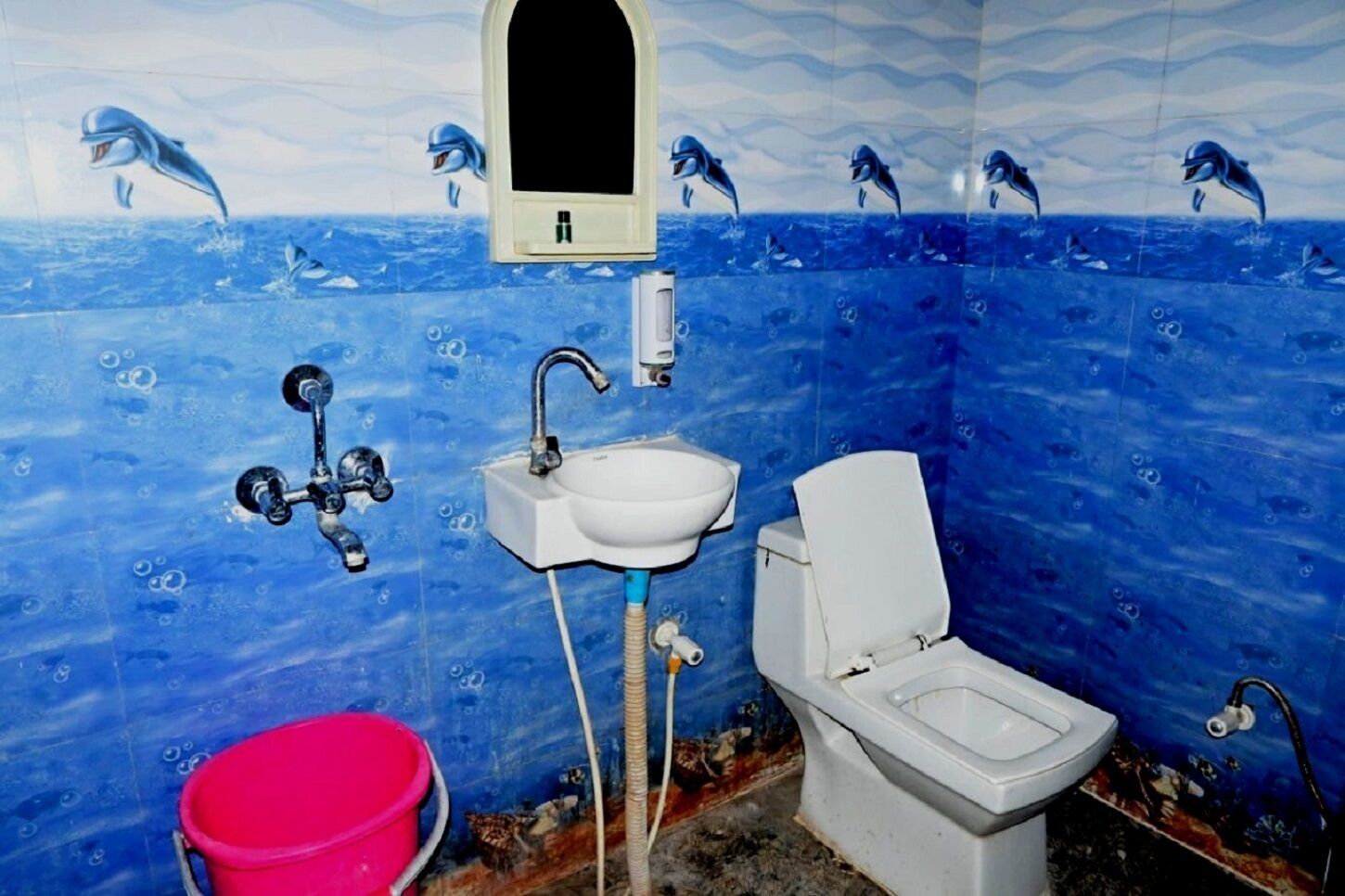 Een badkamer met een blauwe oceaan-thema wand, een witte wastafel, toilet en rode emmer.