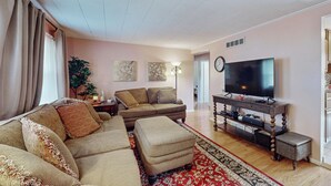 Un salon comprenant un canapé, un pouf, une télévision et un tapis décoratif.