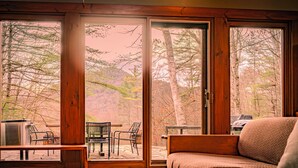 A cozy room with a large window, a wooden bench, and a sofa. - Joia Verde: Mtn Chalet -120 Acres -Adventure Ski Hike MTB Rafting (Charlemont)