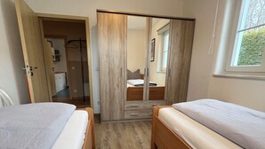 Une chambre avec deux lits, une armoire, une fenêtre et une vue sur la cuisine et la salle de bain.