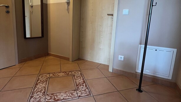 Un couloir avec un sol carrelé, un miroir, une porte et un radiateur.