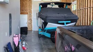 Ett garage med ett träbeklätt tak och väggar, en blå släpvagn och ett svart fordon parkerat inuti.