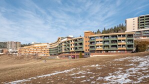 Un hôtel à plusieurs étages, doté de balcons, d’un toit plat et d’une zone herbeuse parsemée de plaques de neige.