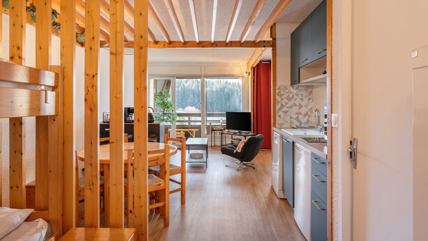 Une pièce aux murs en bois, comprenant une table à manger, des chaises, un canapé, un téléviseur et un coin cuisine avec des placards et un évier.