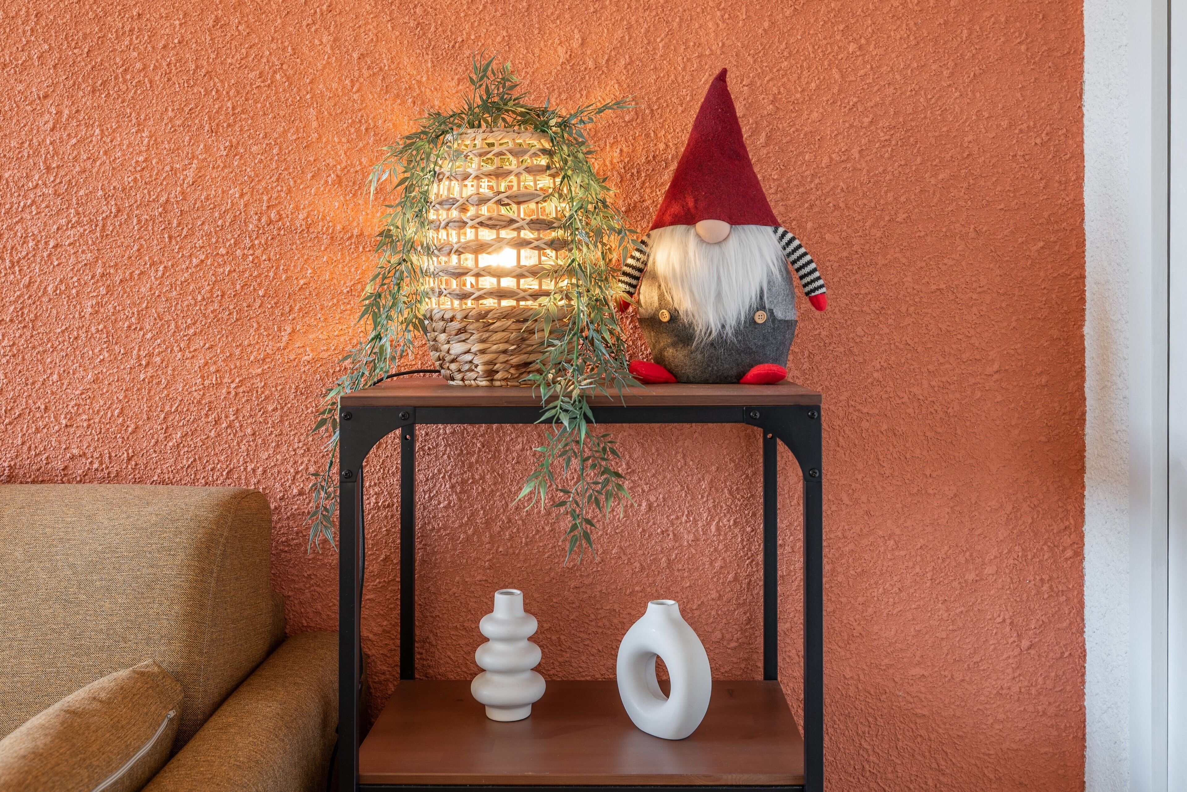 Een klein tuinbeeldje, een geweven lamp en twee vazen op een plank tegen een structuurrijke muur.