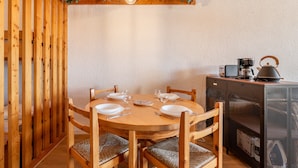 Une table de salle à manger en bois, mise avec des assiettes, des verres et des couverts, entourée de chaises dont les assises sont en osier tressé.