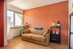 A room with a sofa, a radiator, a window, a plant, and a wall with a textured orange finish. - ‘Évasion Douce Désign’ Apartment with Mountain View, Shared Garden & Wi-Fi (Villard-de-Lans)