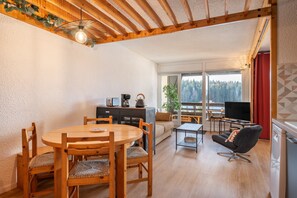 Un tavolo da pranzo in legno con sedie, un divano, una televisione e un balcone con vista sugli alberi.