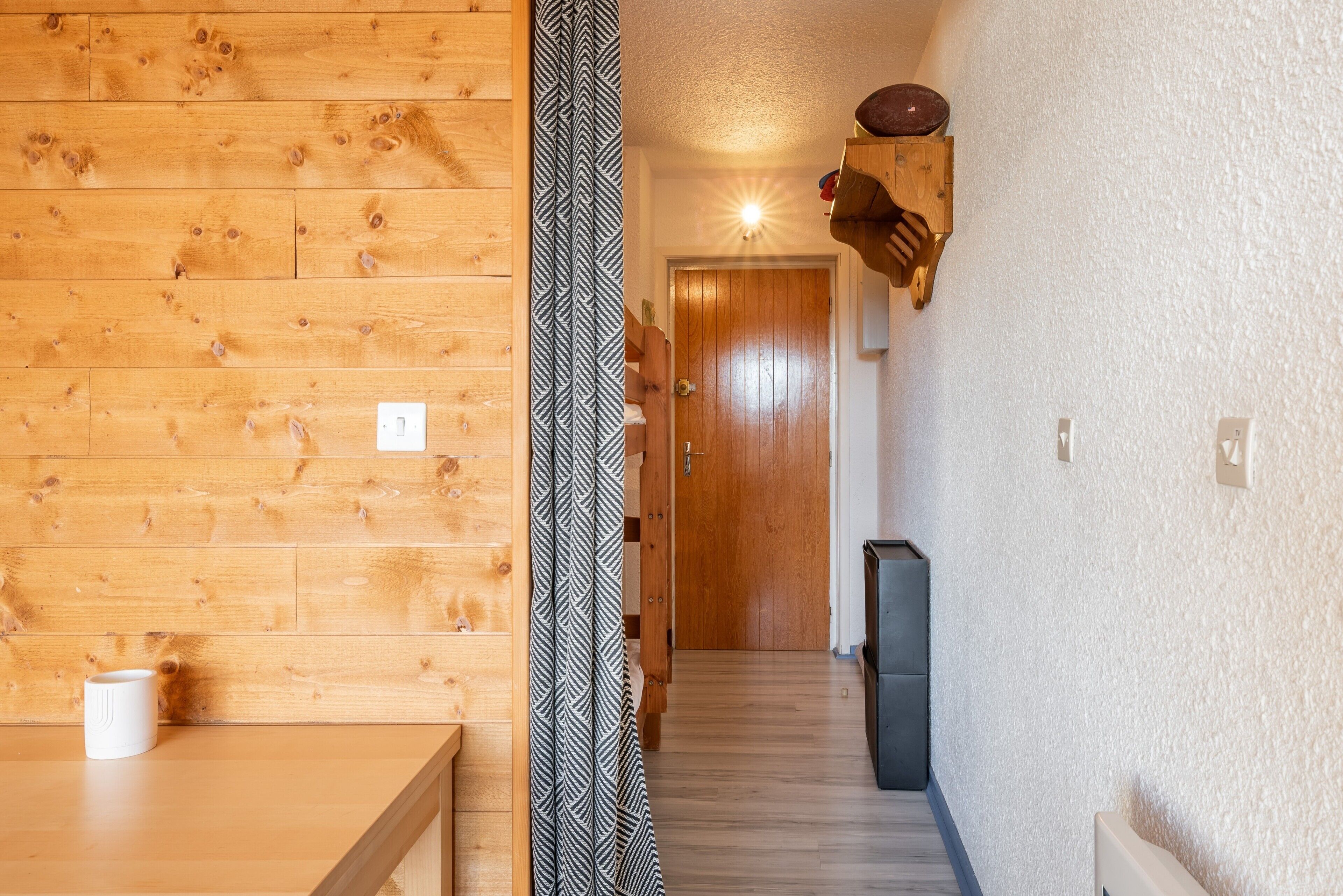 Un intérieur en bois agrémenté d’un rideau à motifs, d’une porte et d’une étagère fixée au mur.