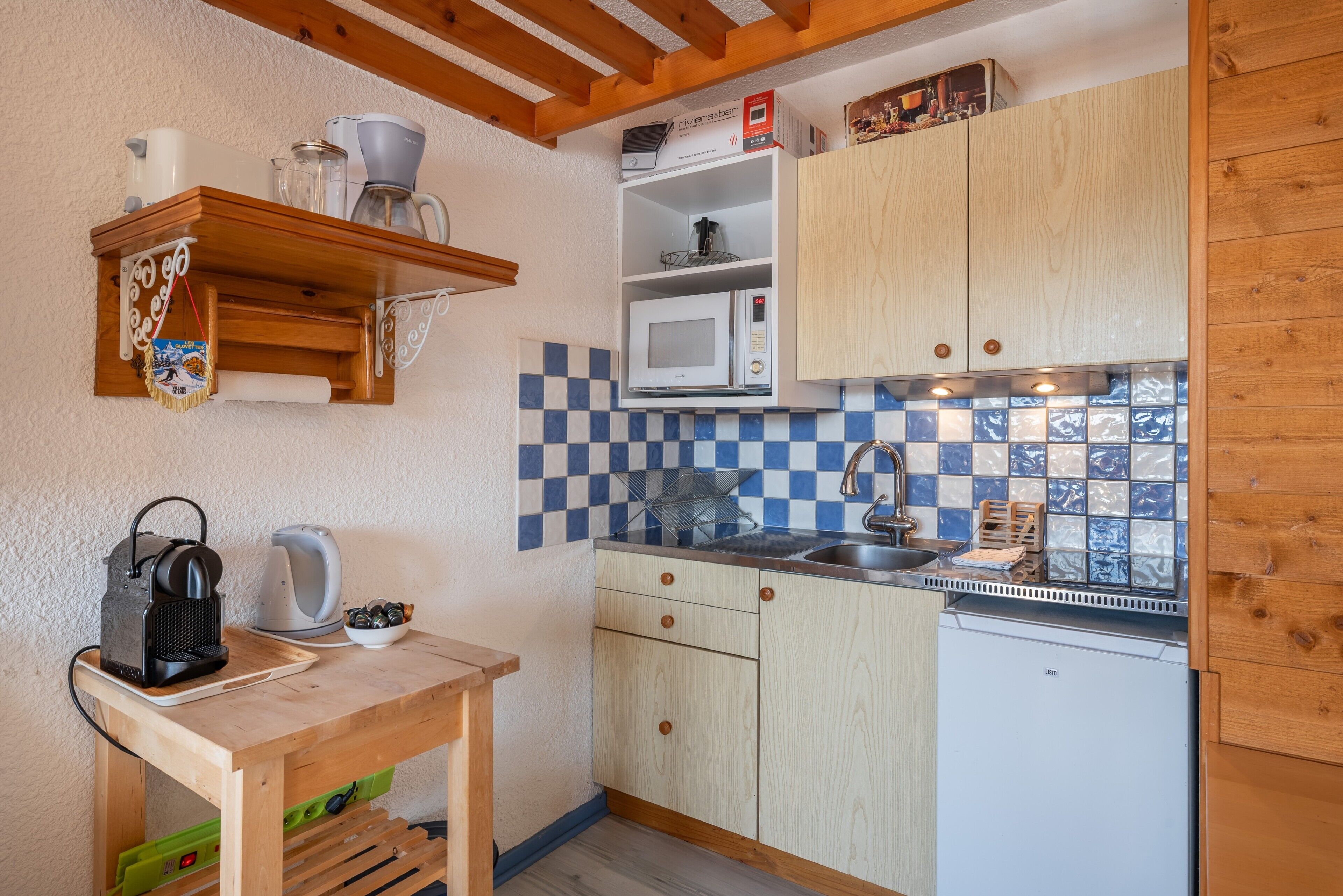 A compact kitchen with wooden cabinets, a microwave, a coffee maker, and a small table.