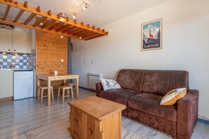Uma sala de estar acolhedora com um sofá marrom, mesa de centro de madeira e uma cozinha com mesa e cadeiras de madeira.