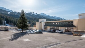 Un estacionamiento con coches, un edificio con techo verde y montañas nevadas al fondo.