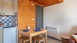 Una cocina compacta con armarios de madera, un salpicadero de azulejos, un refrigerador pequeño y una mesa de comedor con sillas.