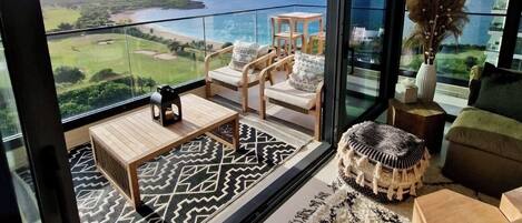 A modern living room with a large glass door leading to a balcony overlooking a golf course and ocean.