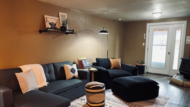 A living room with a dark-colored sofa, a matching ottoman, a patterned rug, and a small side table with a lamp. - Charming 2-BR, no cleaning fees, cozy fireplace (Plains)