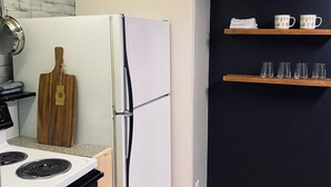 A compact kitchen with a white refrigerator, a stove, and wooden shelves against a dark wall. - Charming 2-BR, no cleaning fees, cozy fireplace (Plains)