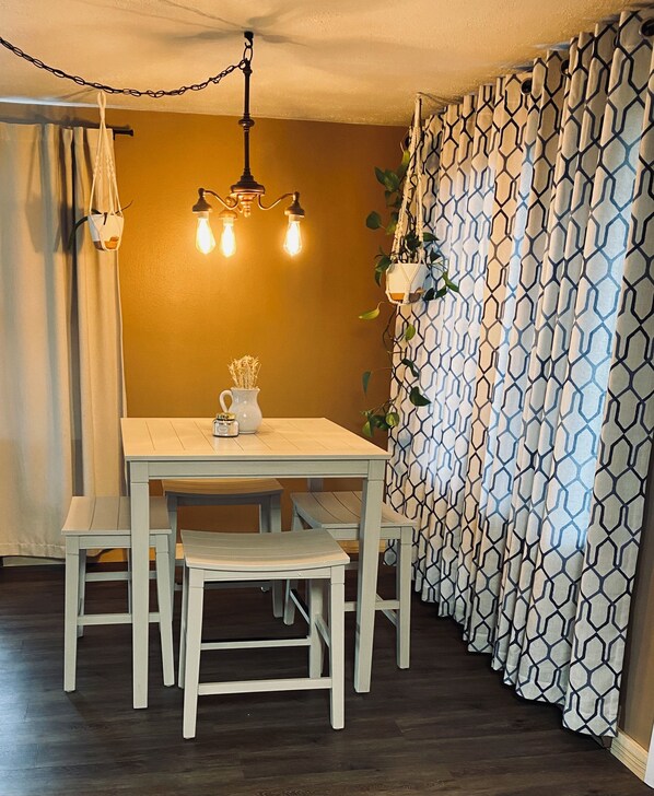 A dining area with a white table and chairs, a hanging light fixture, and patterned curtains.