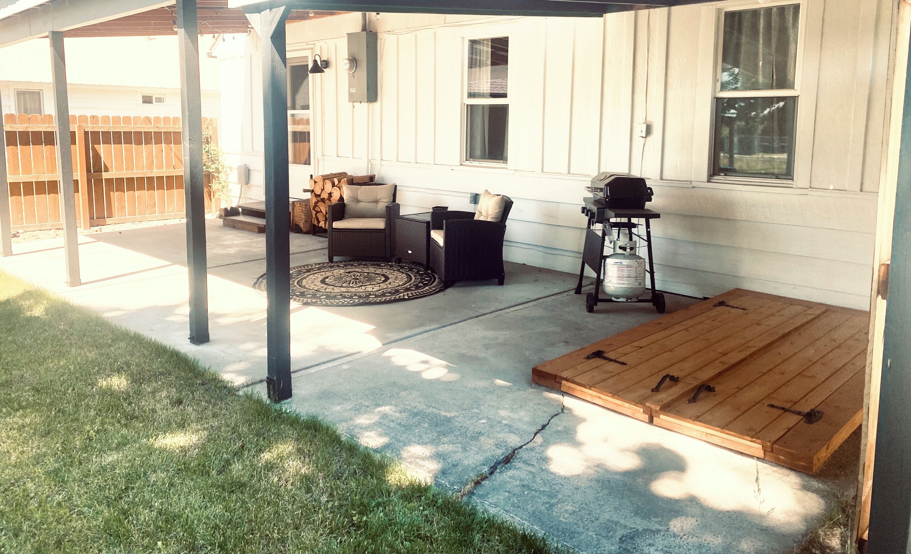 Une terrasse couverte, aménagée avec du mobilier d’extérieur, un barbecue et une bouteille de gaz.
