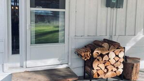 A front door with a glass panel, a wooden bench, and a stack of firewood outside. - Charming 2-BR, no cleaning fees, cozy fireplace (Plains)