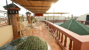 A rooftop terrace with a tiled floor, a covered seating area with a table and chairs, and a decorative brick wall. - EMERALD PALACE (Marrakech)