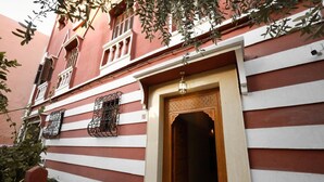 A building with a red and white facade, a wooden door with intricate carvings, and a balcony with metal railings. - EMERALD PALACE (Marrakech)