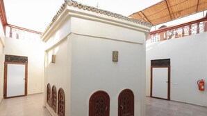 A spacious indoor area with a tiled floor, a central white structure with decorative wooden doors, and a fire extinguisher on the wall. - EMERALD PALACE (Marrakech)