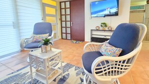 A living room with two wicker chairs, a small table with a plant, and a television on the wall.