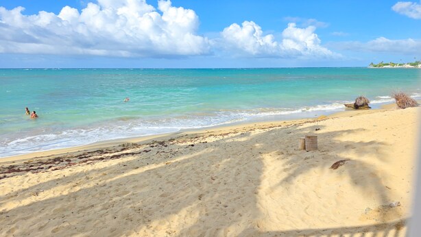 A beach with clear turquoise water, a sandy shore, and a few people swimming.