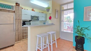 Uma cozinha com armários brancos, um micro-ondas, uma geladeira e dois bancos brancos.