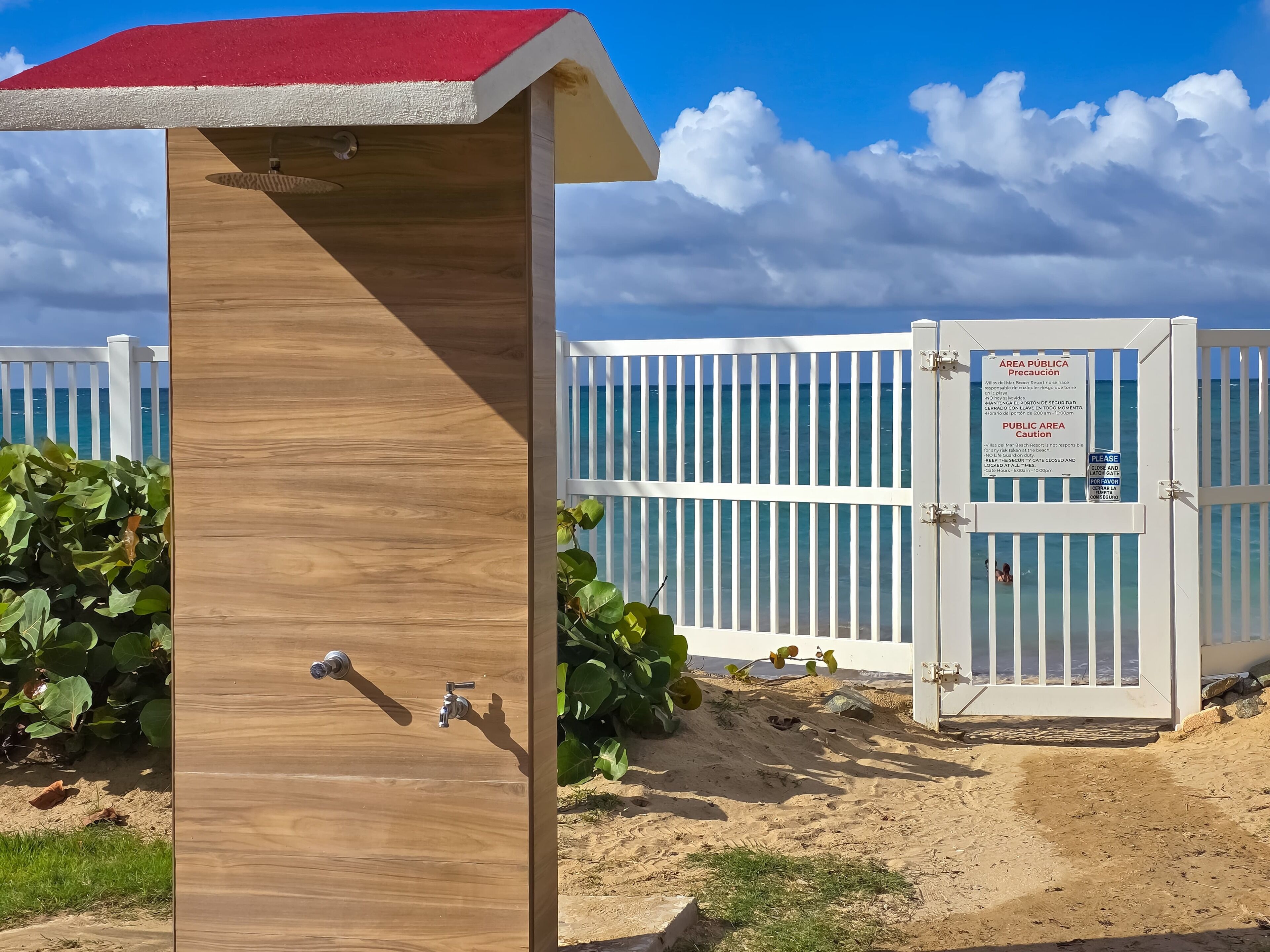 A wooden structure with a red roof, a white fence, and a sign indicating a public area caution.