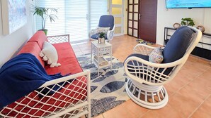 Uma sala de estar com sofá, cadeira, televisão e ventoinha no teto.
